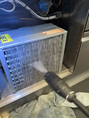 AC evaporator coil being cleaned with compressed air spray gun during maintenance service in NYC