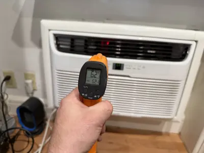 Infrared thermometer reading 62°F confirming proper cooling output from installed window AC unit in NYC