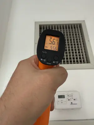 Technician using infrared thermometer to verify AC vent output temperature reading 56°F in NYC