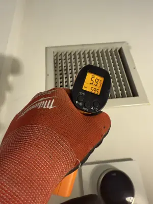 Technician using infrared thermometer to check HVAC vent temperature during appliance diagnostics