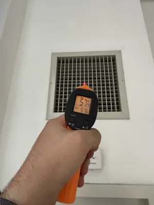 Technician using infrared thermometer to measure air vent temperature during HVAC inspection in NYC