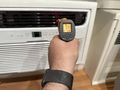 Technician using infrared thermometer to verify AC unit cooling output during installation in NYC