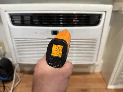 Infrared thermometer reading 55°F air output confirming successful window AC installation in NYC apartment