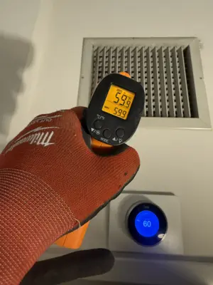 Technician using infrared thermometer to verify HVAC vent output at 59°F with Nest thermostat set to 60°F