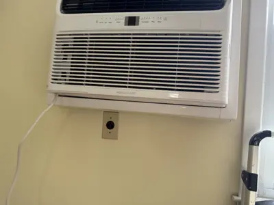 Frigidaire window AC unit professionally installed in a NYC apartment wall with power outlet below