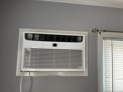 Frigidaire window AC unit cleanly installed in NYC bedroom window with neat trim and blinds nearby