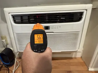 Technician testing Frigidaire window AC unit output temperature with infrared thermometer showing 56°F