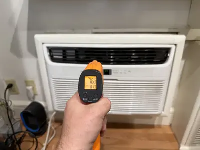 Infrared thermometer verifying AC unit output temperature at 76 degrees after installation in NYC