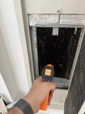 Technician using infrared thermometer to test AC unit temperature reading during NYC installation