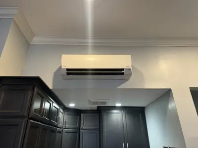Newly installed mini-split AC unit mounted high on kitchen wall above dark wood cabinetry in NYC home