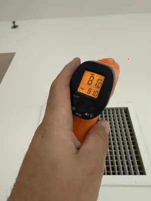 Technician using infrared thermometer to verify AC vent temperature reading 81°F in NYC home