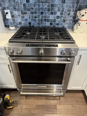 stainless steel kitchenaid gas range installed in a modern nyc kitchen with white cabinets and blue tile backsplash