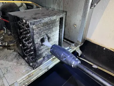 Technician pressure washing a heavily soiled commercial refrigerator evaporator coil during cleaning service in NYC