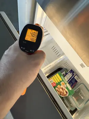Technician using infrared thermometer to check refrigerator temperature reading at 48 degrees during appliance diagnostic