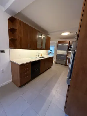 Fully renovated NYC kitchen with wood cabinets, stainless fridge, dishwasher, and white countertops