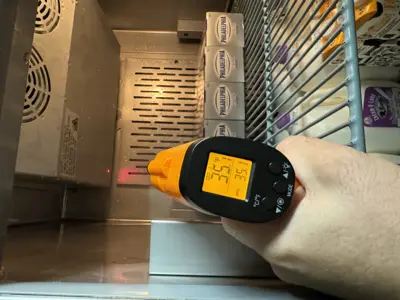 Technician using infrared thermometer to check commercial refrigerator temperature in NYC