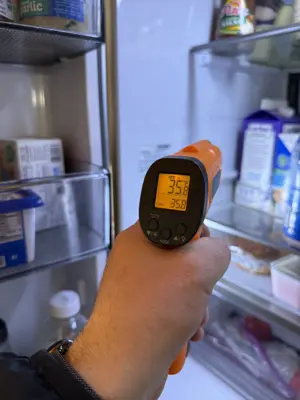 Technician using infrared thermometer to diagnose refrigerator temperature issue during appliance repair