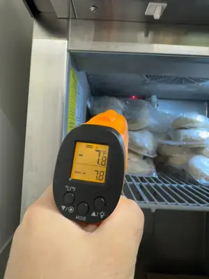 Technician using infrared thermometer to check commercial refrigerator temperature during repair in NYC