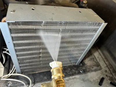 AC condenser coil being cleaned with water spray during commercial appliance service in NYC