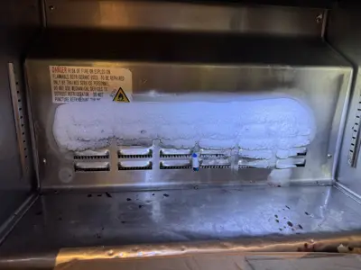 Heavily frost-covered evaporator coils inside a commercial refrigerator before defrost repair service in NYC