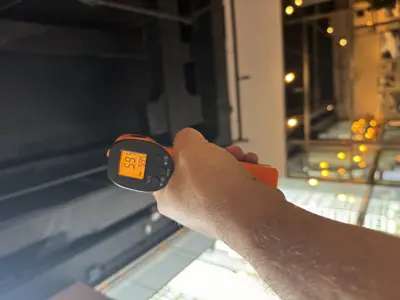 Technician using infrared thermometer to measure temperature inside commercial refrigeration unit during repair