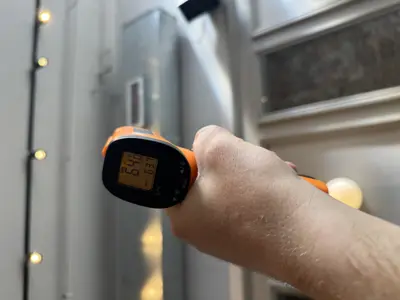 Technician using infrared thermometer to check refrigerator temperature during appliance diagnostic in NYC