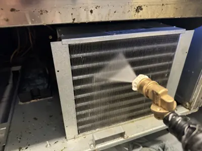 Technician pressure washing commercial refrigerator condenser coils during deep cleaning service in NYC