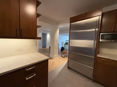 Large stainless steel refrigerator installed in a renovated NYC kitchen with dark wood cabinets