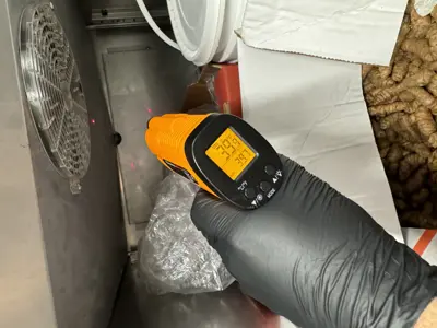 Technician measuring internal temperature of commercial refrigeration unit fan area with infrared thermometer