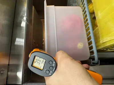 Technician using infrared thermometer to measure temperature inside commercial refrigeration unit during repair