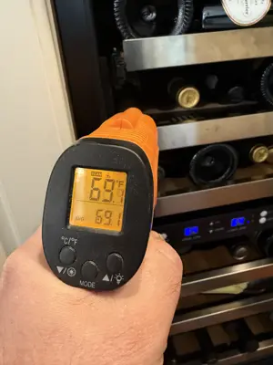 Technician using infrared thermometer to check wine cooler temperature at 69°F in NYC home