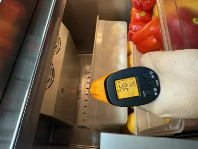 Infrared thermometer confirming 36°F temperature inside a commercial refrigerator stocked with fresh produce