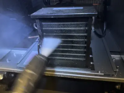 Technician steam cleaning refrigerator evaporator coils during professional appliance repair service in NYC