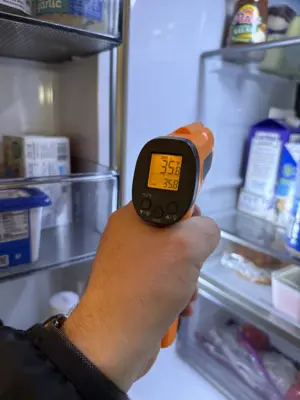 Technician using infrared thermometer to check refrigerator temperature during appliance diagnostic
