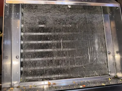 Heavily clogged and dirty AC or refrigerator condenser coils covered in dust and debris before cleaning