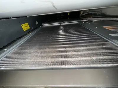 Close-up of commercial refrigeration condenser coil fins showing buildup requiring professional cleaning
