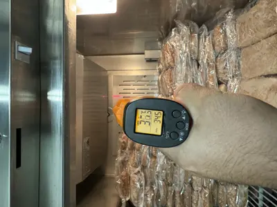 Technician using infrared thermometer inside commercial walk-in cooler showing 34°F temperature reading