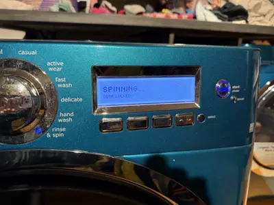 Teal front-load washing machine displaying SPINNING cycle on digital screen after repair service in NYC