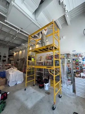 Handyman on scaffolding installing ceiling light fixtures in a commercial space in NYC