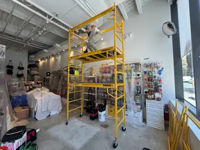Handyman on scaffolding working on ceiling electrical or lighting installation in NYC commercial space