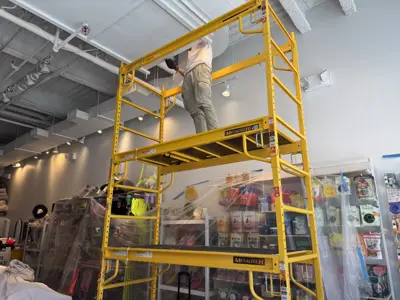Handyman on scaffolding installing ceiling light fixture in NYC commercial space