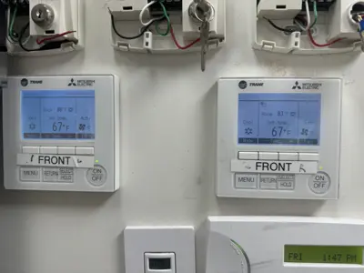 Dual Mitsubishi Electric Trane HVAC thermostats installed and operational on white wall in NYC