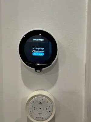 Nest smart thermostat installed and configured on white wall alongside HunterDouglas blind controller in NYC