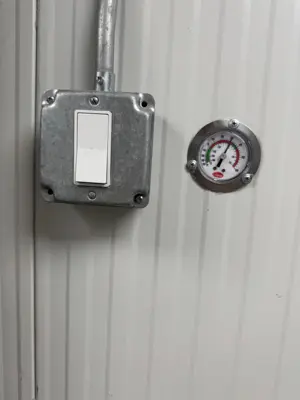 Installed industrial wall switch box and pressure gauge on corrugated metal wall in NYC