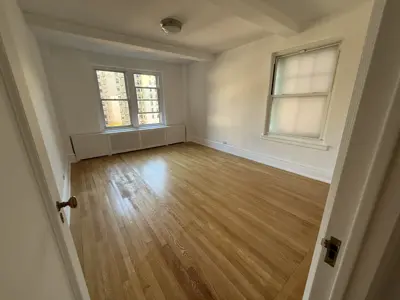 Refinished hardwood floors in bright empty NYC apartment bedroom with white walls and trim