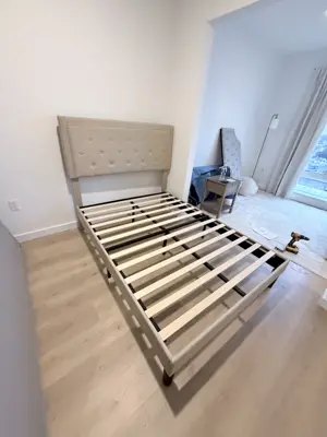 Fully assembled upholstered queen bed frame with tufted headboard in a bright NYC bedroom