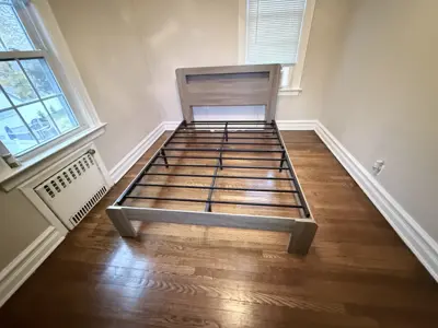 Fully assembled twin bed frame with headboard on hardwood floor in a bright NYC bedroom