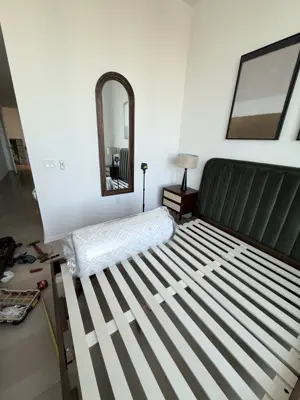 Bed frame assembly in progress with green upholstered headboard in NYC bedroom