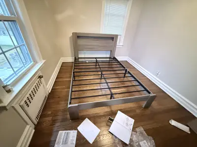 Completed bed frame assembly with grey wood headboard on hardwood floor in NYC bedroom
