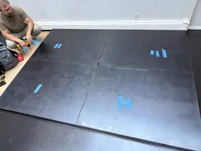 Handyman assembling large dark platform bed frame panels with drill in NYC apartment